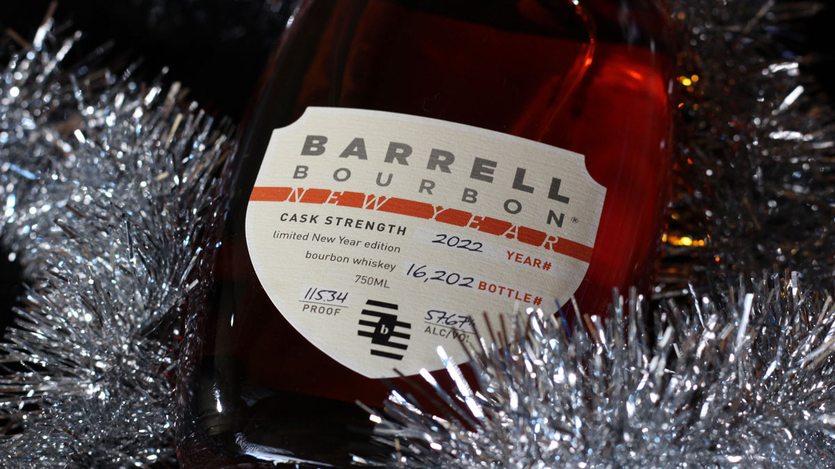 A bottle of Barrell Bourbon New Year 2022 lying on a table with a garland of silver sparkles surrounding it.