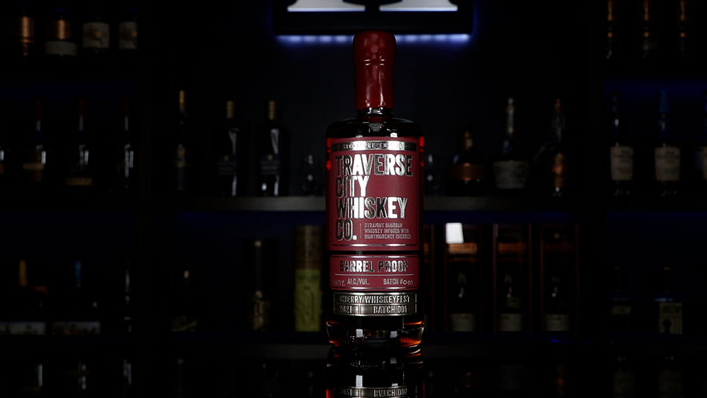 A bottle of TC Whiskey Co.'s Barrel Proof Cherry Limited Release sitting on a table in front of shelves filled with bottles. The Homebar logo is illuminated in the background.