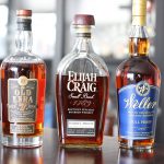 Three bottles stand next to each other on a table. On the left is Old Ezra 7 Barrel Strength, Center is Elijah Craig Barrel Proof and right is Weller Full Proof.