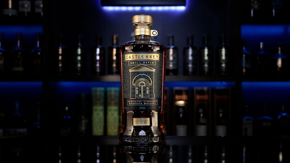 A bottle of Castle & Key's Small Batch Bourbon sits on a table in the center of the camera frame.