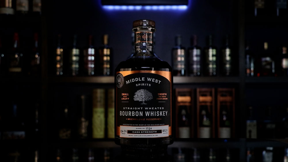 A bottle of Middle West Spirits' Straight Wheated Bourbon Whiskey in front of a Homebar logo sign.