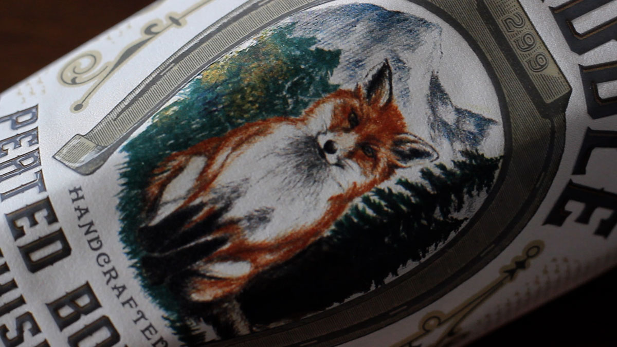 A close up of the bottle label for J. Riddle Peated Bourbon. It features an illustration of a fox in front of trees and mountains.