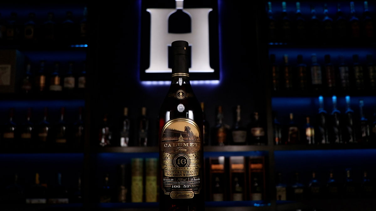 A bottle of Calumet Farm 16 Year Single Rack Black Kentucky Straight Bourbon Whiskey sits in front of a lit up sign of the Homebar.io logo.