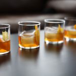 5 Old Fashioned cocktails sit on a black table with a leather couch in the background.