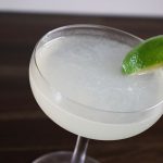 A Daquiri rests in a coupe glass, garnished with a lime wedge stuck on the edge of the glass.