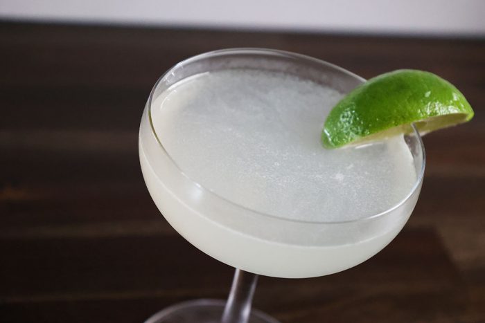 A Daquiri rests in a coupe glass, garnished with a lime wedge stuck on the edge of the glass.
