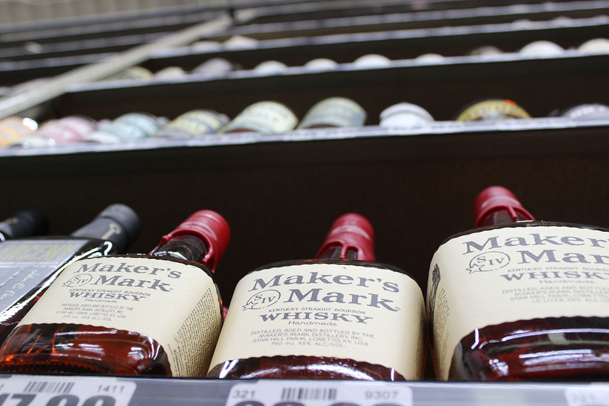 A bottle of Maker's Mark Bourbon Whiskey sits on a shelf in a liquor store.