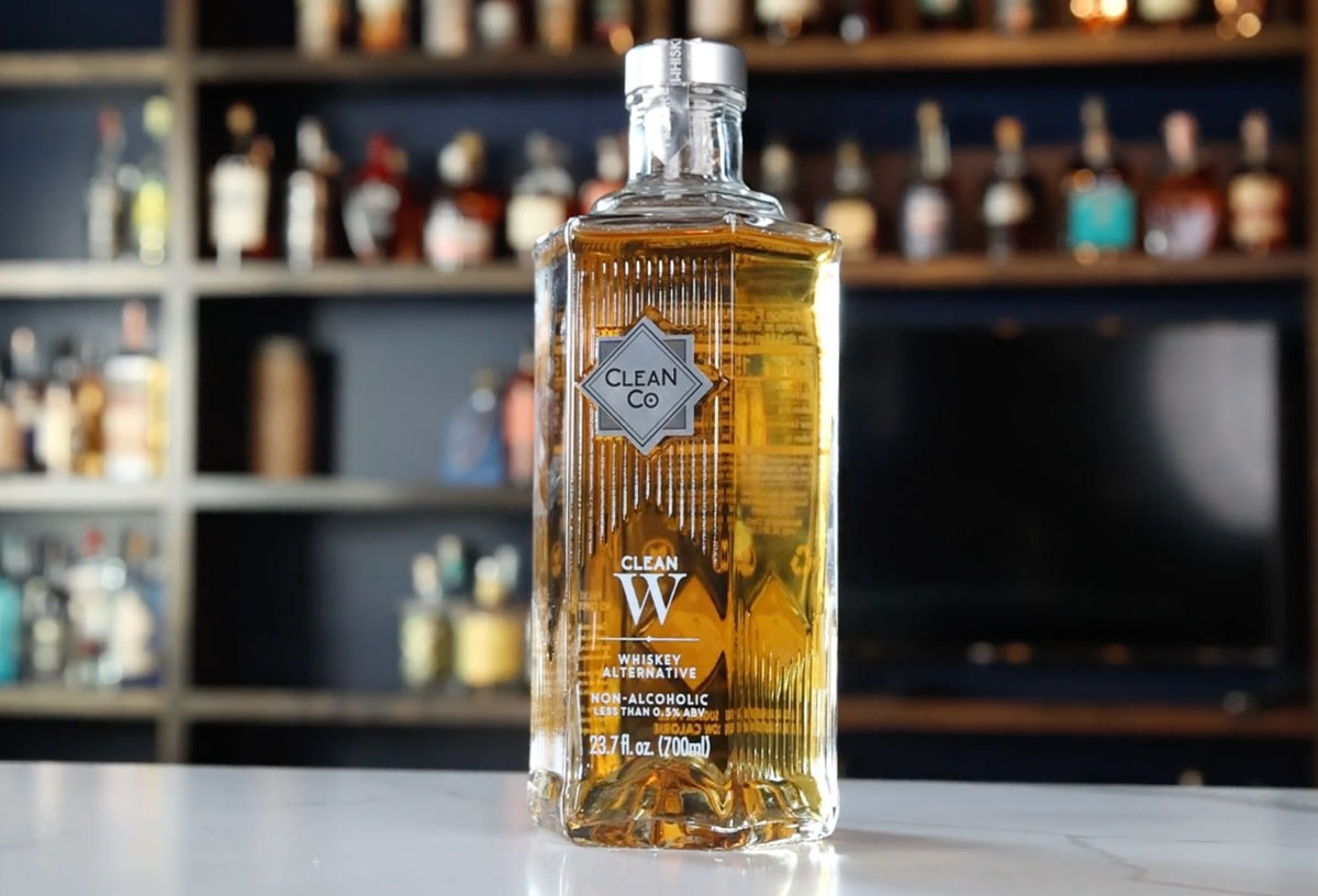 A bottle of Clean Co.'s Whiskey Alternative sits in front of shelves of liquor bottles.