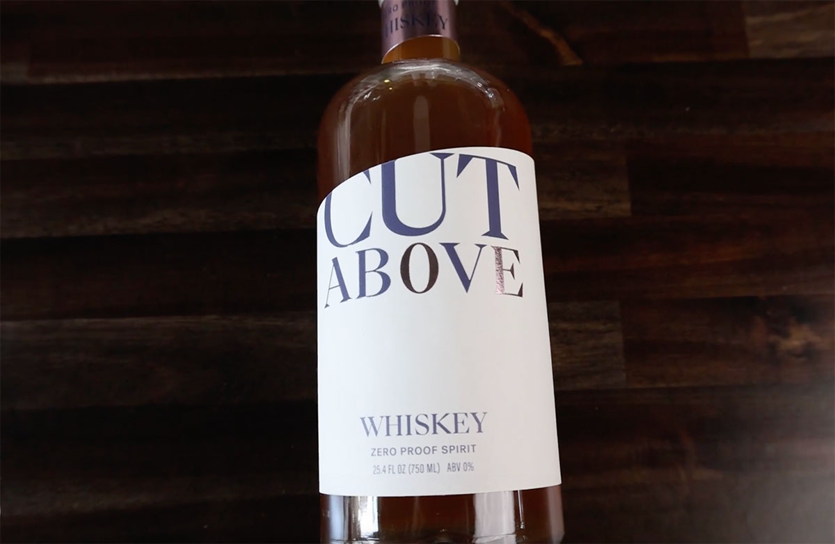 A bottle of Cut Above Spirits' Zero Proof Whiskey sits on a dark butcher block surface.