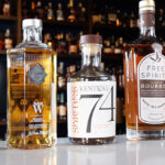 Several non-alcoholic whiskey bottles sit next to one another on a bar top.