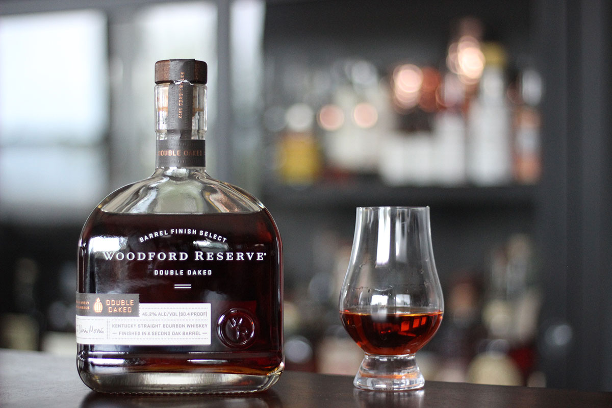 A bottle of Woodford Reserve Double Oaked sits next to a Glencairn tasting glass with an ounce of whiskey in it.